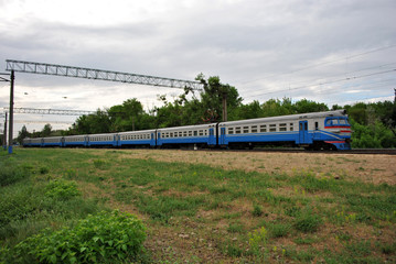 Blue train, railroad along trees line, horizontal composition,  spring cloudy day in Ukraine