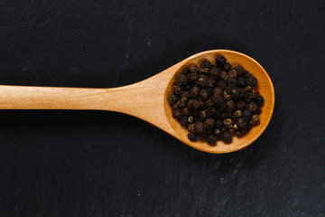 Black pepper spice in wooden spoon on dark stone table
