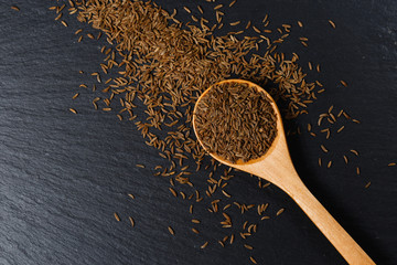 Cumin spice in wooden spoon on dark stone table