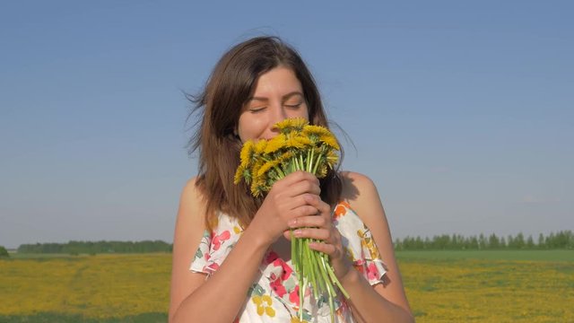 Portrait of Woman In Field With Bouquet of Yellow Dandelion Flowers Sniffing Him