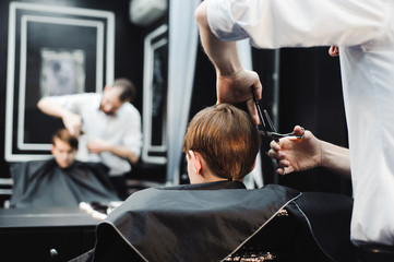 Cute little boy is getting haircut by hairdresser at the barbershop