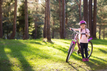 Happy child in a protective helmet before riding a bike in the Park. Active leisure for children. girl holding a bicycle and smile