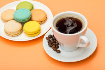 Cup of coffee with coffee beans and delicious macarons cakes of different color on white porcelain plate
