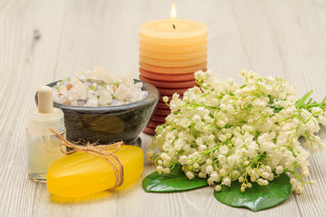 Obraz na płótnie Canvas Soap, bottle with aromatic oil, bowl with sea salt, burning candle and bouquet of lilies of the valley