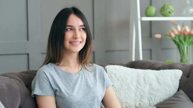 Beautiful young woman resting on sofa at home. Portrait of smiling girl looking at camera