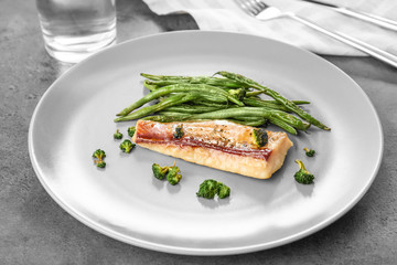 Plate with tasty fish and green beans on table