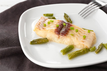 Plate with tasty fish and green beans on table