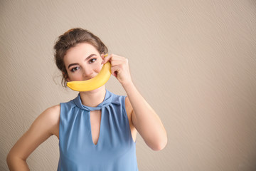 Funny portrait of young woman with banana on color background