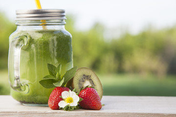 glass of detox smoothie and fruit on wooden table in the garden with fruit