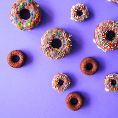 Chocolate baked doughnuts on a violet background glazed and decorated with confetti. Top view. Square image.