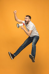 Jumping fan on orange background. The young man as soccer football fan with megaphone