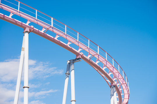 Pink pastel looping roller coaster on blue sky sunny day background.