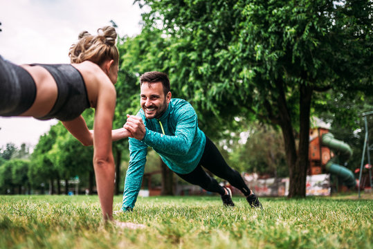 Young couple doing one hand push-up exercise in the park.