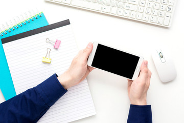 white Desk, male hands, guy holding a white smart phone, notebook, pen, white background with copy space, for advertisement, top view