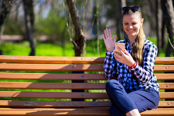 Beautiful female person making video call to boyfriend by phone. Concept of communicating with close people by wireless Internet. Concept of speaking by modern gadgets and fast Internet in park