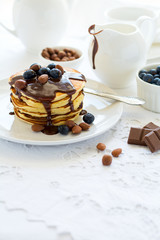 Traditional breakfast concept. Stack of pancakes with chocolate sauce, blueberries and nuts on white table cloth. Selective focus