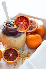 Jar of fresh smoothie with orange, blueberry and granola on white wooden salver