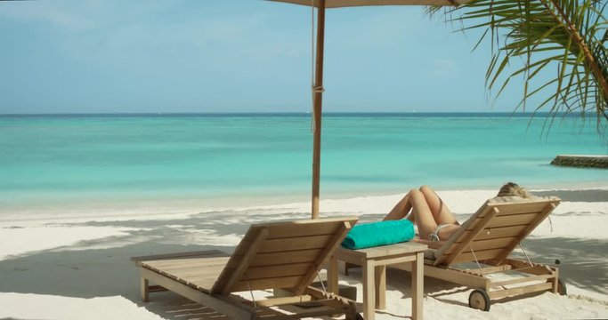 Close-up of Beautiful Blonde Female Lying on the Deck Chair on the Beach. Sunbathing on the Exotic Location with Turquoise Sea in the Background. Shot on RED Epic 4K UHD Camera.