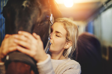 Young woman hugging her horse in stables before a ride - Powered by Adobe