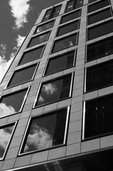 Black and white image looking up at a modern, city building with reflections in the windows