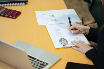 Working woman writing on her paper sheet and disscuss with her colleague with laptop, smartphone, diary, paper sheet and coffee cup on the desk.