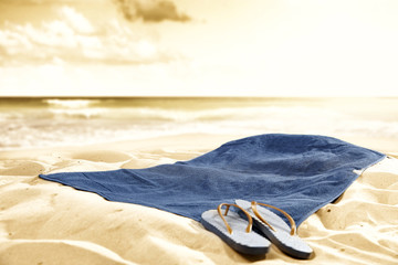 Summer flip-flops on blue towel on sandy beach with blurred bright sea and sky background in summer...