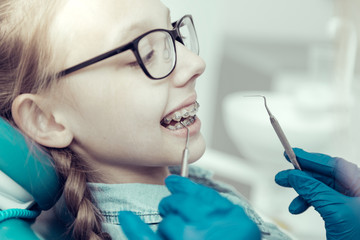 Braces off. Cute little girl in braces sitting in a dental clinic while her dentist holding necessary tools