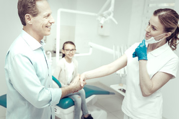 Fototapeta na wymiar Thank you. Happy smiling grateful patient shaking hands with his experienced professional dentist in a modern dental clinic