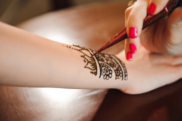 Master mehndi draws henna on a female hand.
