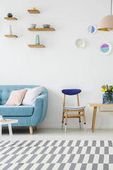 Cropped photo of a sofa, wooden chair, table, striped carpet and shelves with decoration on the wall in a living room interior