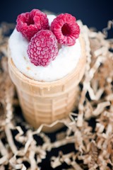 Ice cream with raspberry in waffle cone on wood