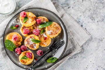 Healthy summer breakfast, cheese pancakes with raspberry, powdered sugar and mint, grey concrete background copy space