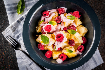 Ukrainian, Russian food, lazy vareniki; Curd or cheese gnocchi with fresh raw raspberries, cream and mint, on a dark concrete background, copy space top view