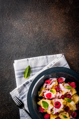 Ukrainian, Russian food, lazy vareniki; Curd or cheese gnocchi with fresh raw raspberries, cream and mint, on a dark concrete background, copy space top view