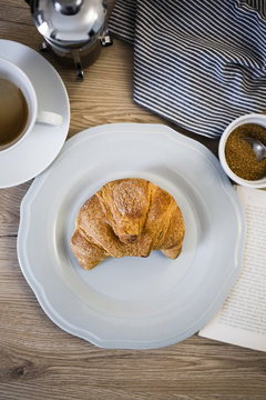 Italian cornetto on plate, book, serviette and coffee cup