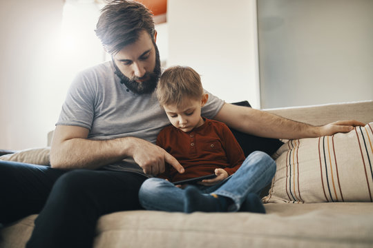 Father and son sitting on couch, looking at smartphone