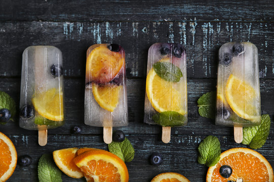Homemade detox popsicles with blueberries, orange slices and mint leaves on black wood