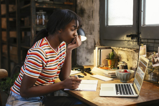 Pensive young woman sitting at desk in a loft looking at laptop