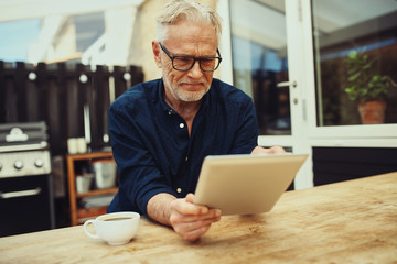 Smiling senior man holding a tablet and drinking coffee outside