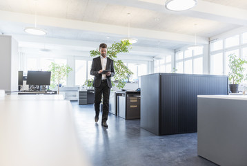 Businessman walking in office, using digital tablet