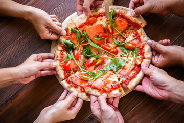 Yummy pizza with smoked salmon and vegetables on a wooden table background. The customers or friend...