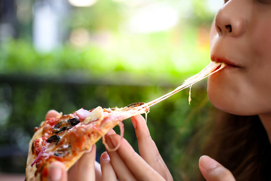 Pizza look so yummy or delicious food. Charming beautiful asia woman is eating pepperoni pizza and sticky mozzarella cheese. Attractive girl feels hungry and loves the taste. She sit at restaurant