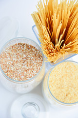 Spaghetti in the form of a bouquet in a transparent vase, next to transparent containers with buckwheat and rice