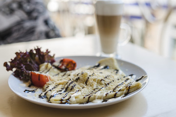 Crepe with cheese and tomatoes in a white plate on the summer terrace