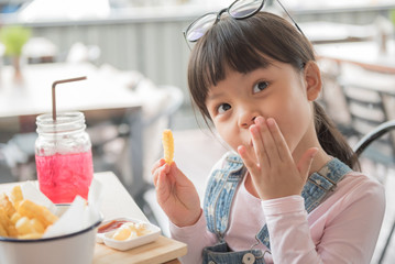 Beautiful laughing little girl sitting at table and eating French fries from your plate.