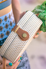 Woman hands with fashionable stylish rattan bag outside. Tropical island of Bali, Indonesia. Rattan and silk.