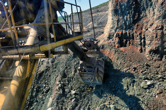 excavator bucket digs rock in an iron ore quarry