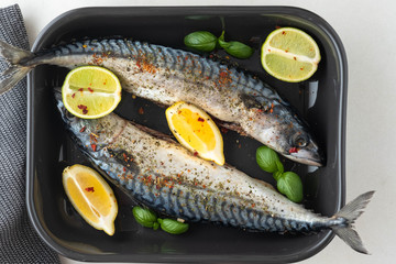 Two fresh mackerels in a black ceramic bowl with condiments. Upper plane.
