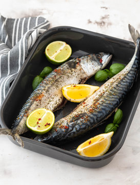 Two fresh mackerels in a black ceramic bowl with condiments. Upper plane.
