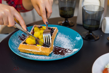 Woman hands cutting belgium waffles with mango and blueberry